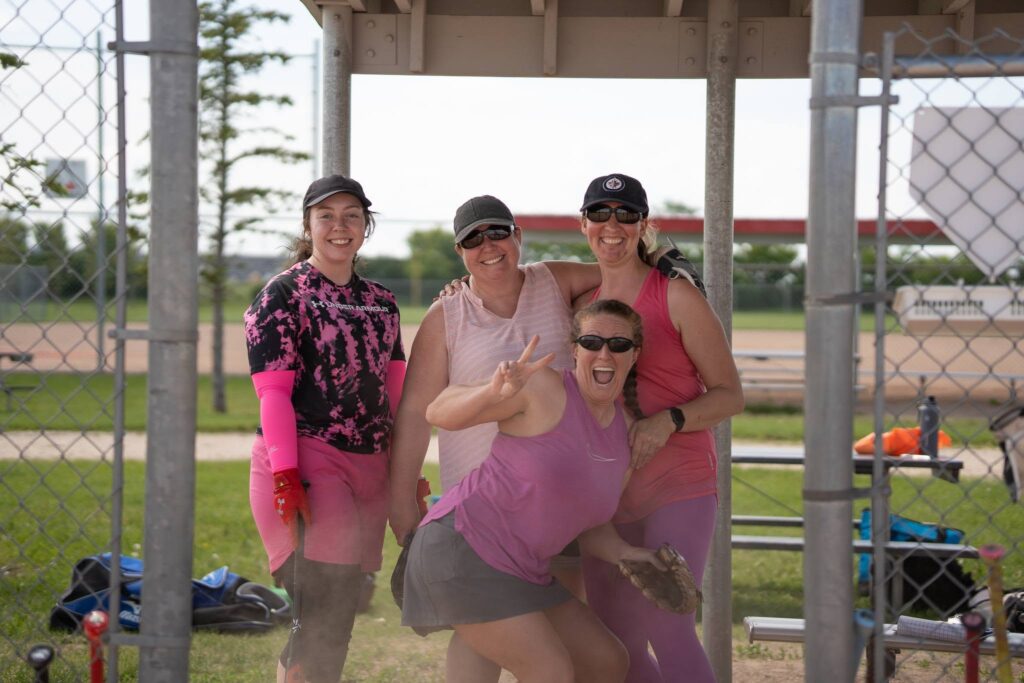 A group of four people smile as they wait for their turn to bat.