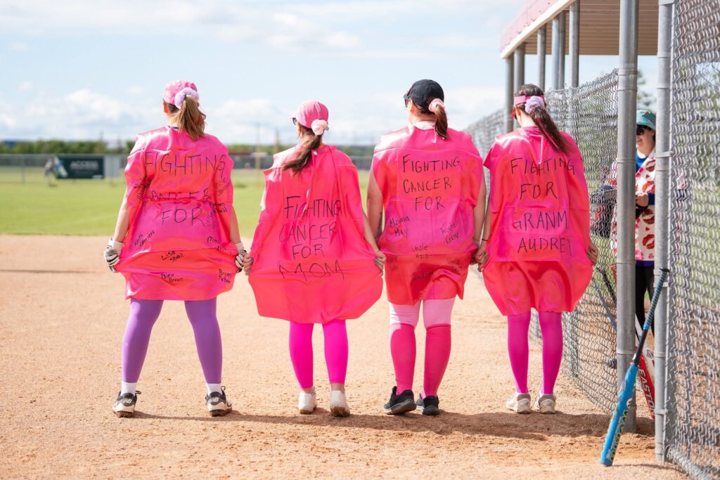 Four people with the reasons they're fighting for cancer written on the backs of their pink T-shirts.