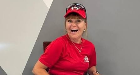 A woman wearing an umpire uniform sits in a chair laughing.