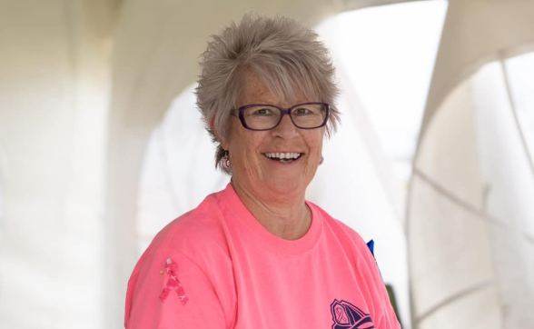 A woman with white hair and red glasses smiling.